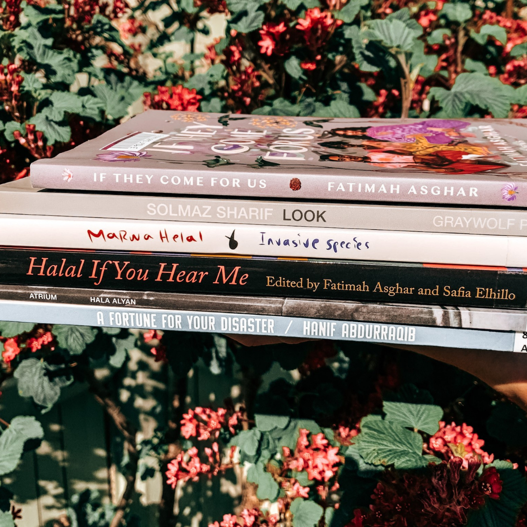 A stack of poetry collections by Muslim writers held against a currant tree.